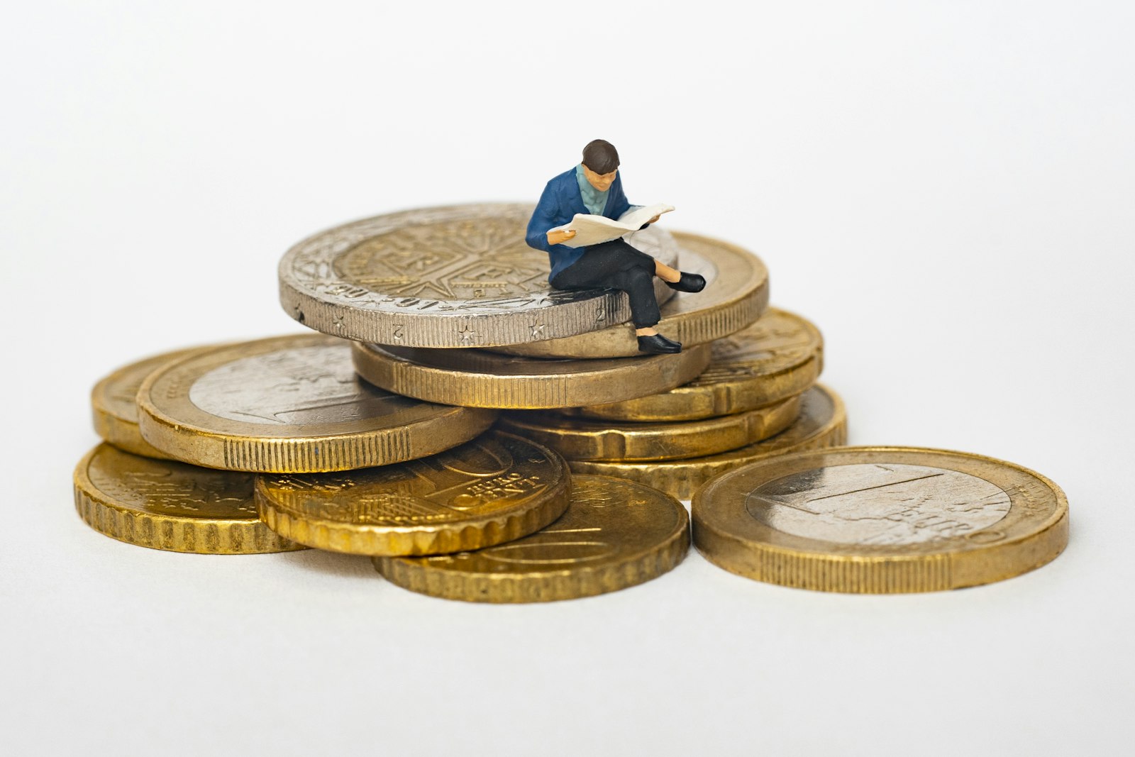 Kleine Figur liest ein Blatt auf einem Stapel Euro-Münzen