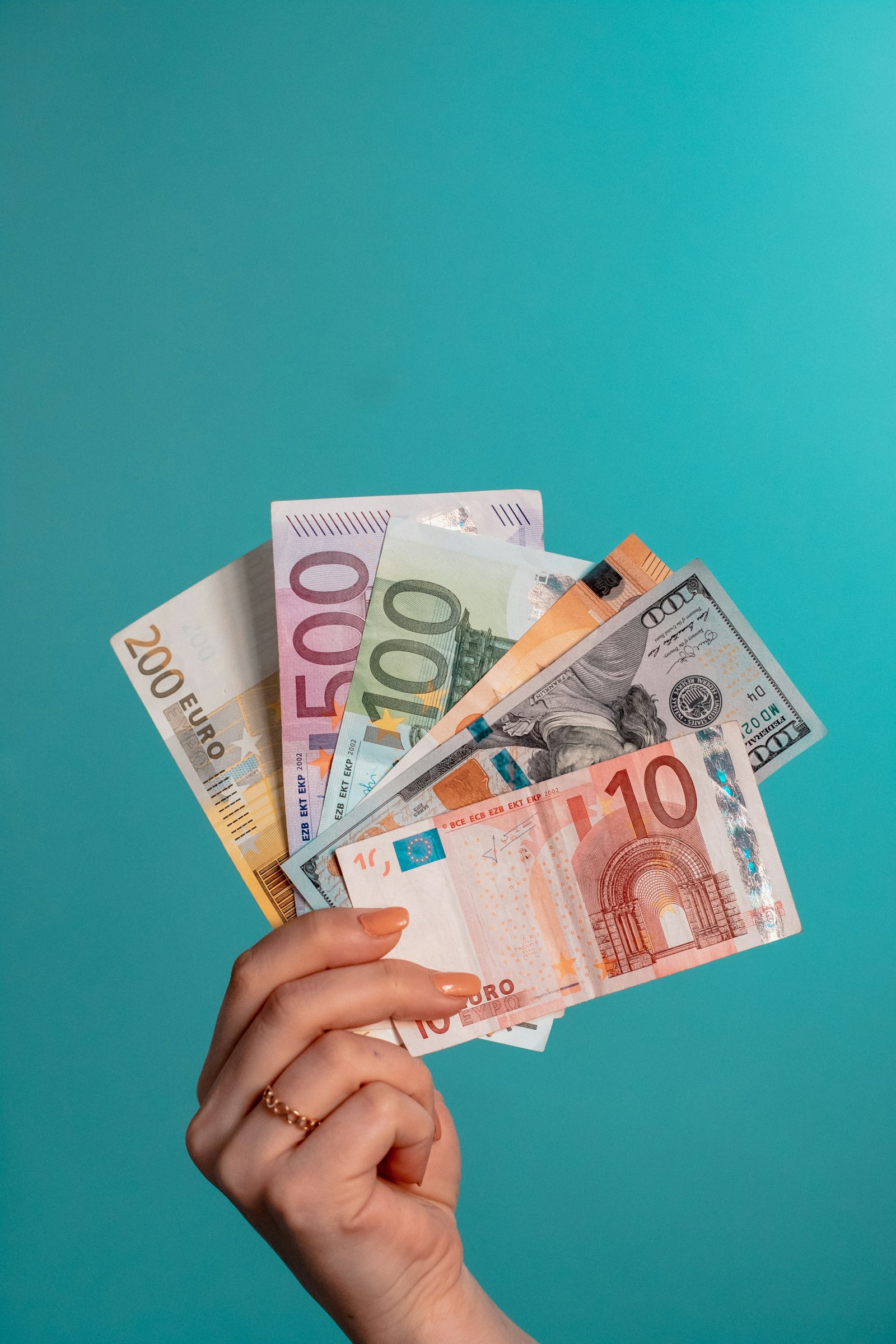 Eine Hand hält Euro- und Dollarnoten vor einem türkisen Hintergrund